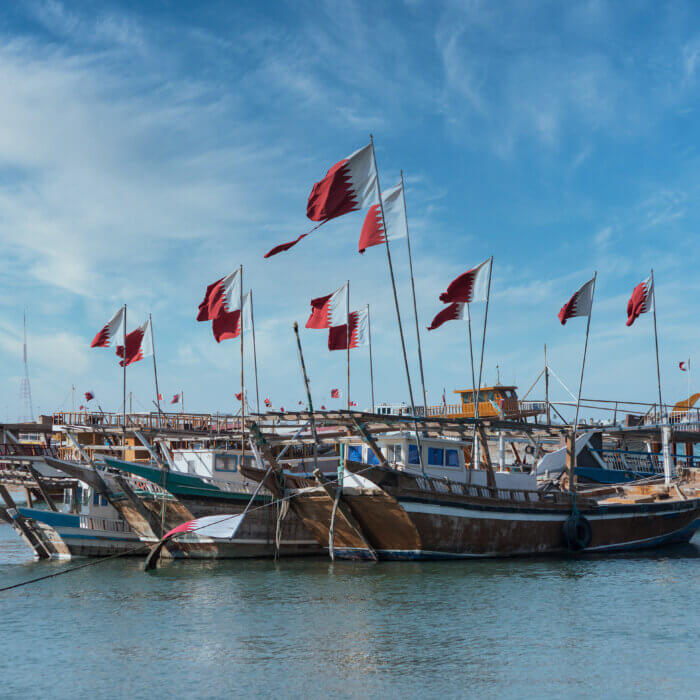 Image shows Qatar flag and traditional boats in Doha