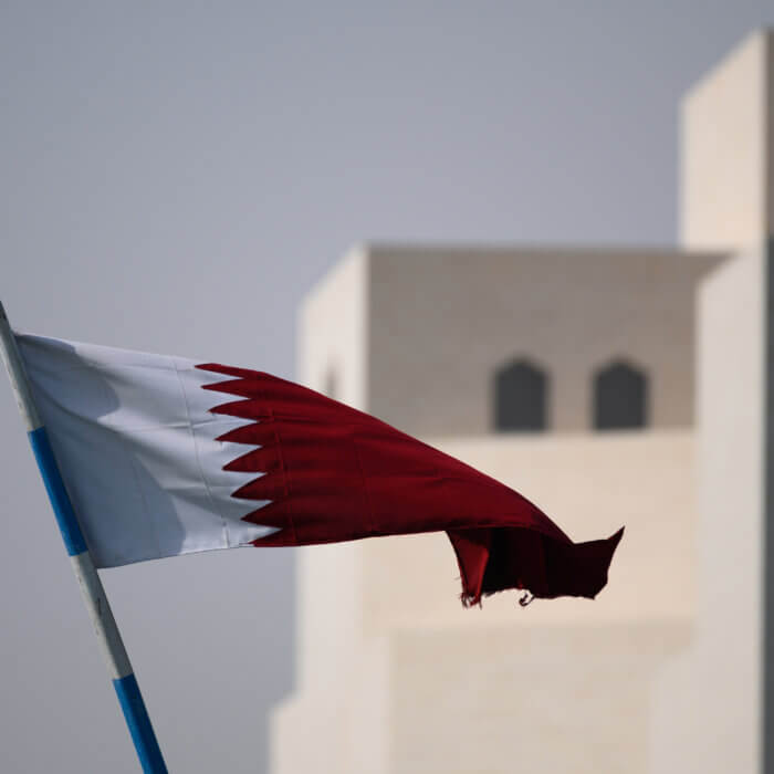 Image shows Qatar flag with building behind