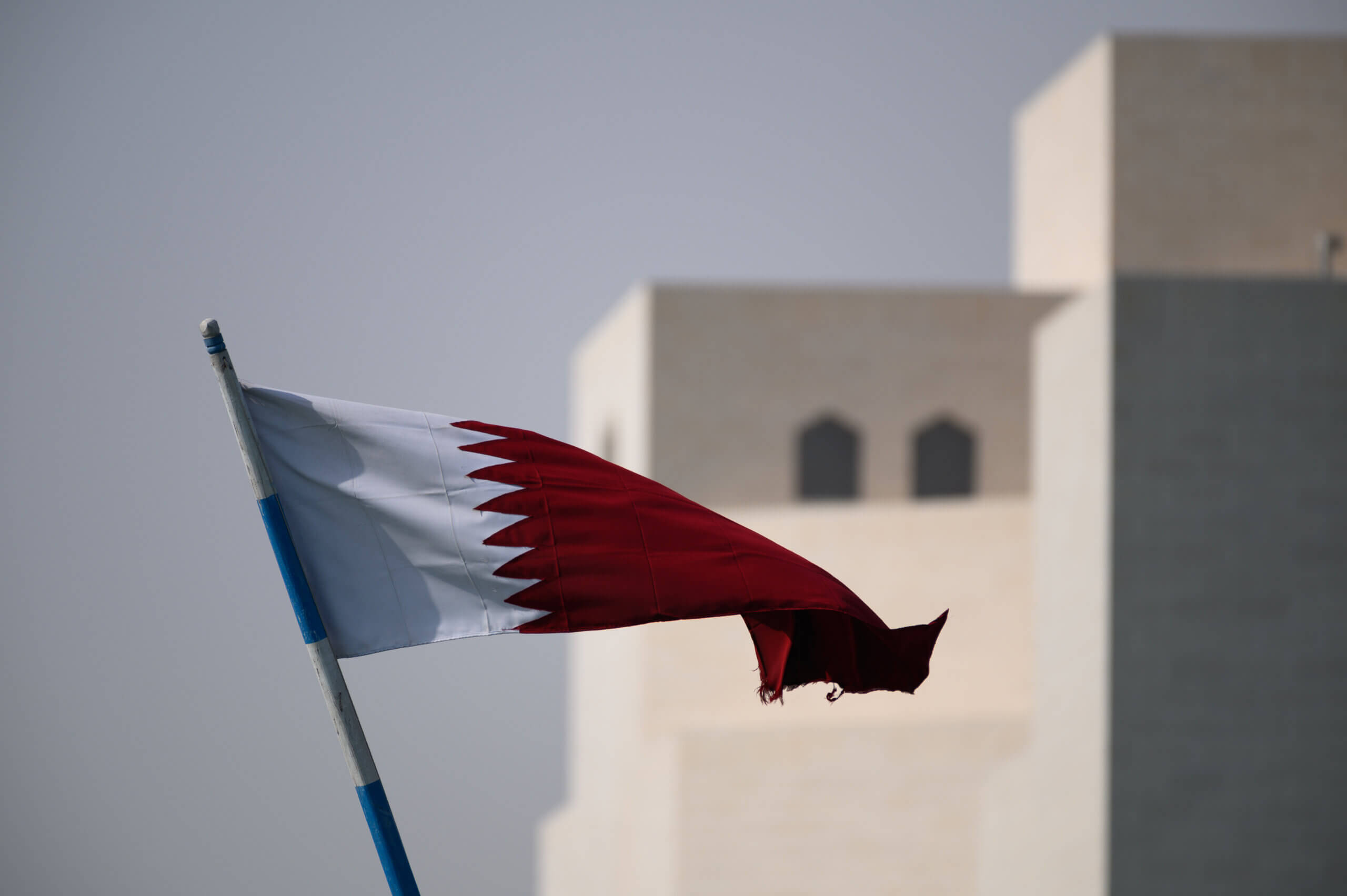 Image shows Qatar flag with building behind