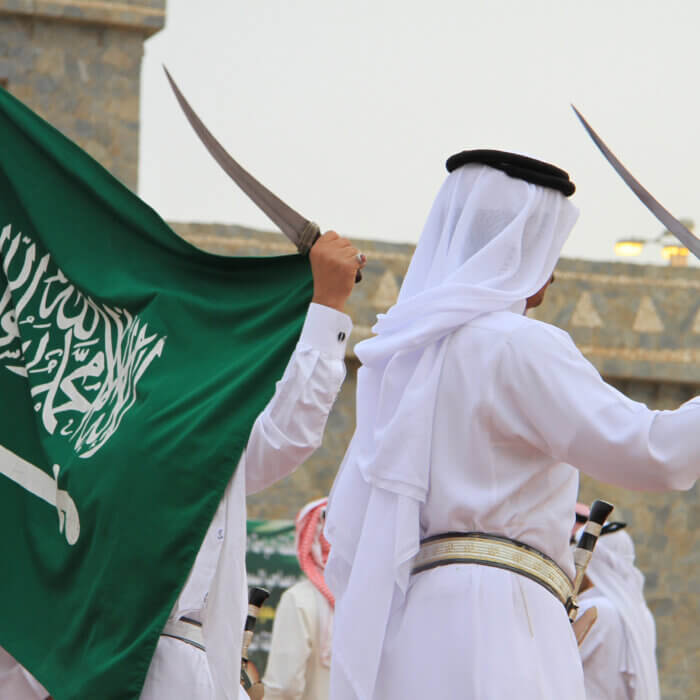 Saudi men with swords dancing near Saudi flag