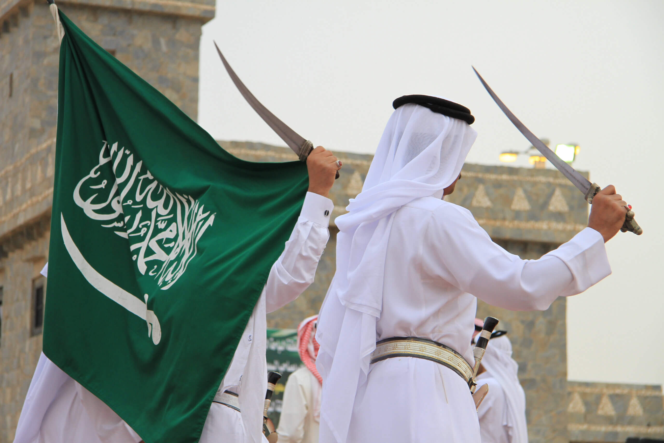 Saudi men with swords dancing near Saudi flag